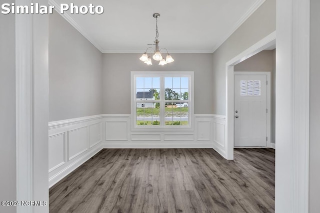 unfurnished dining area with hardwood / wood-style flooring, crown molding, and an inviting chandelier