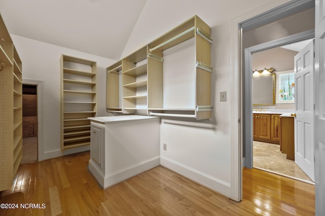 walk in closet with light wood-type flooring, vaulted ceiling, and sink