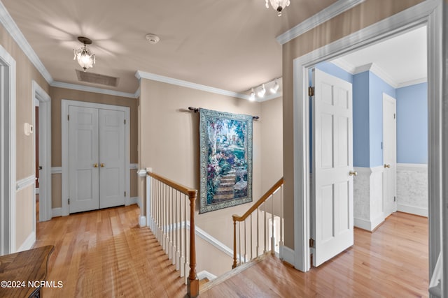 hallway with light wood-type flooring, track lighting, and ornamental molding