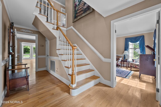 staircase featuring a healthy amount of sunlight, ornamental molding, and hardwood / wood-style flooring