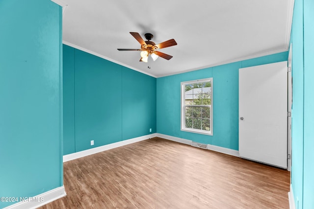 empty room featuring a ceiling fan, wood finished floors, visible vents, and crown molding