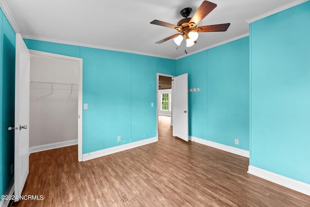 unfurnished bedroom with baseboards, ornamental molding, wood finished floors, a walk in closet, and a closet