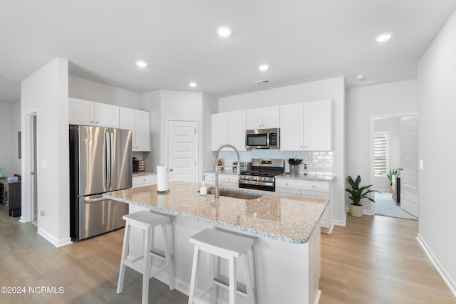 kitchen with appliances with stainless steel finishes, white cabinets, decorative backsplash, a kitchen island with sink, and light stone countertops