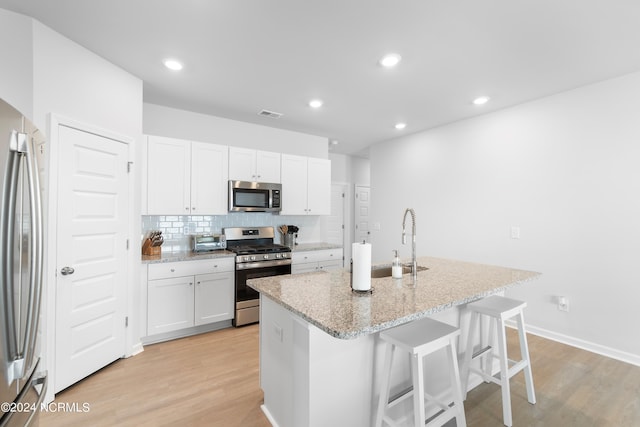 kitchen with appliances with stainless steel finishes, white cabinetry, a breakfast bar area, a kitchen island with sink, and light stone counters