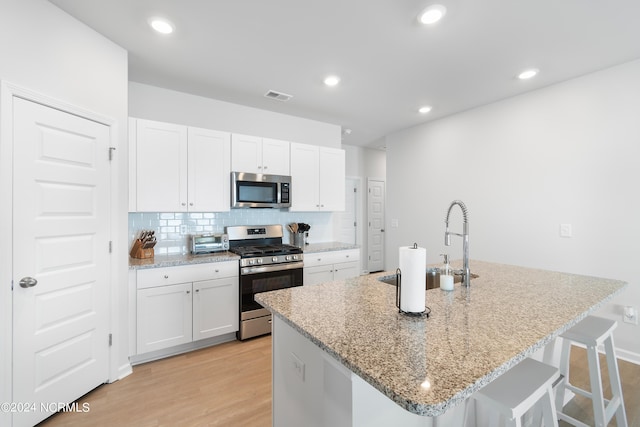 kitchen featuring stainless steel appliances, a center island with sink, and white cabinets