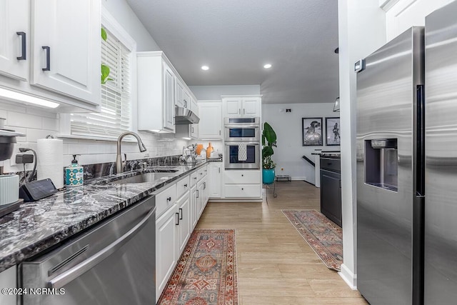 kitchen featuring sink, dark stone countertops, appliances with stainless steel finishes, decorative backsplash, and white cabinets