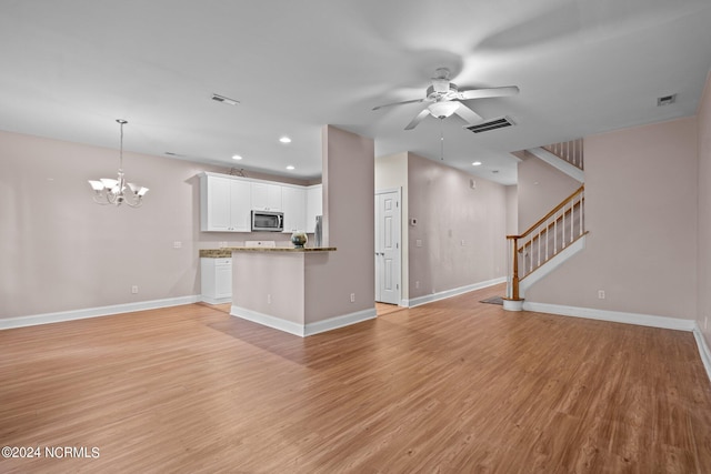 unfurnished living room with stairs, ceiling fan with notable chandelier, light wood-type flooring, and baseboards