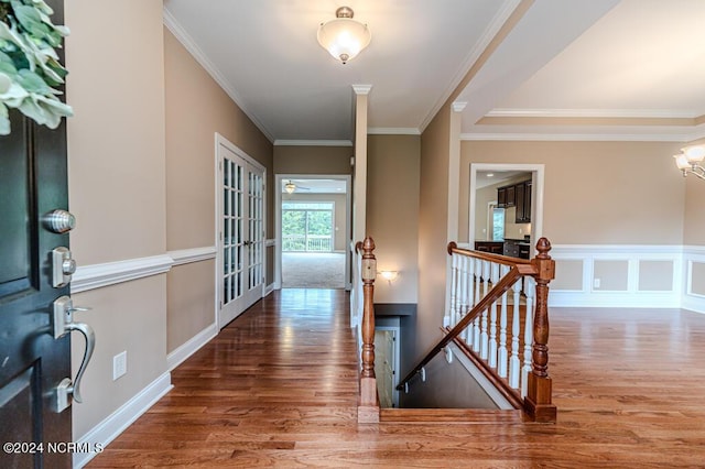 corridor with a decorative wall, wood finished floors, an upstairs landing, and crown molding