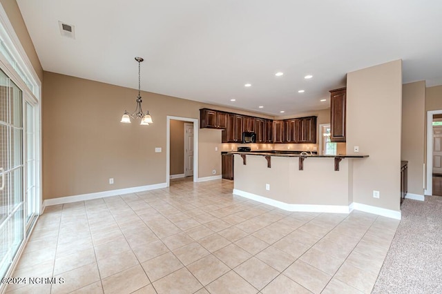 kitchen with visible vents, an inviting chandelier, black microwave, a peninsula, and a kitchen breakfast bar