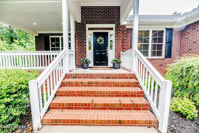 view of exterior entry with brick siding and a porch