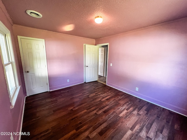 unfurnished bedroom with multiple windows, dark hardwood / wood-style flooring, ornamental molding, and a textured ceiling