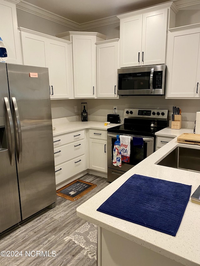 kitchen featuring sink, white cabinets, hardwood / wood-style flooring, ornamental molding, and stainless steel appliances