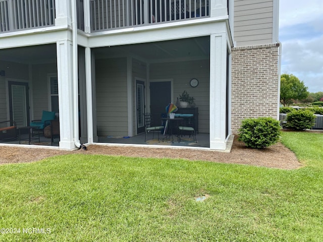 doorway to property with a balcony, a patio area, and a lawn