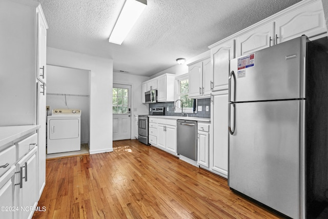 kitchen featuring appliances with stainless steel finishes, light hardwood / wood-style flooring, white cabinets, and washer / dryer