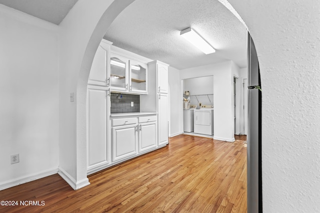 kitchen with washing machine and dryer, white cabinets, light hardwood / wood-style flooring, and tasteful backsplash