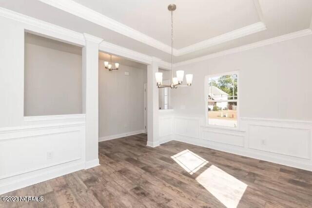 unfurnished dining area with crown molding, ornate columns, an inviting chandelier, dark wood-type flooring, and a tray ceiling