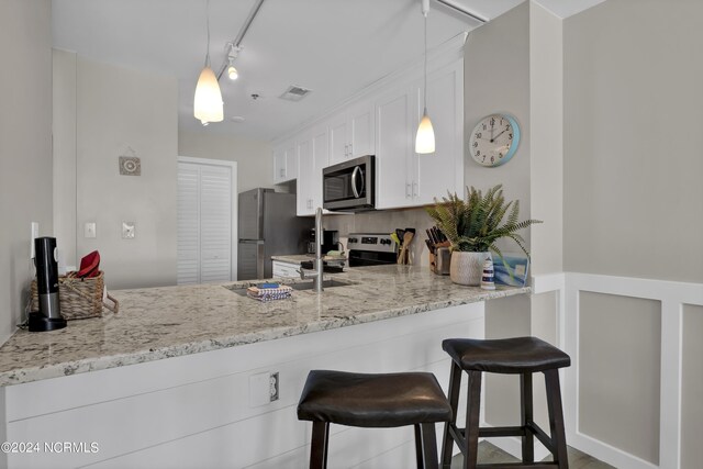 kitchen with white cabinetry, stainless steel appliances, pendant lighting, rail lighting, and backsplash