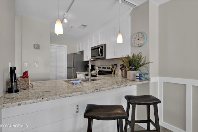 kitchen featuring light stone counters, stainless steel appliances, white cabinets, track lighting, and a peninsula