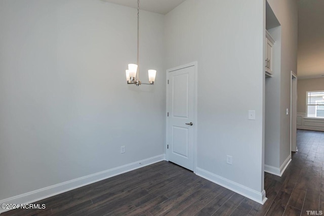 unfurnished room with a notable chandelier, dark wood finished floors, and baseboards