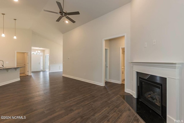 unfurnished living room with baseboards, dark wood finished floors, a glass covered fireplace, high vaulted ceiling, and ceiling fan with notable chandelier