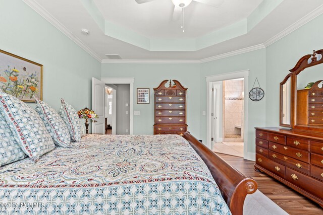 bedroom with ceiling fan, wood-type flooring, ensuite bathroom, and a tray ceiling