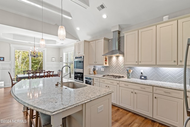 kitchen featuring backsplash, sink, light wood-type flooring, and wall chimney range hood