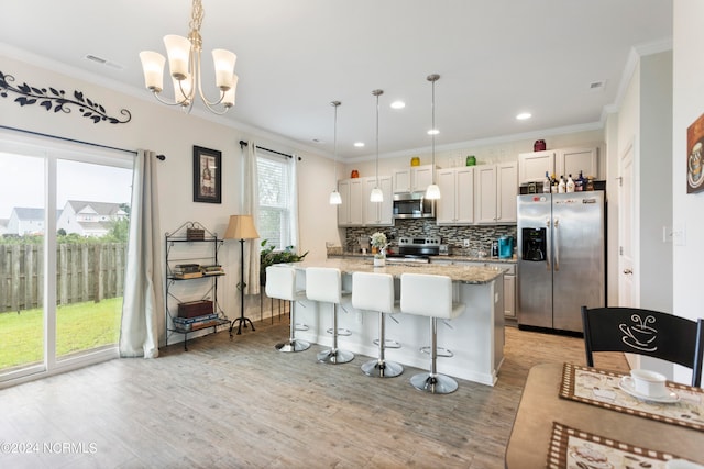 kitchen featuring appliances with stainless steel finishes, decorative light fixtures, an island with sink, and a breakfast bar