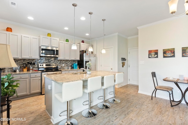 kitchen featuring stainless steel appliances, light hardwood / wood-style floors, an island with sink, and pendant lighting