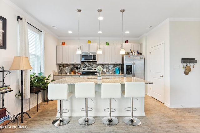 kitchen featuring a kitchen island with sink, stainless steel appliances, hanging light fixtures, and light stone countertops