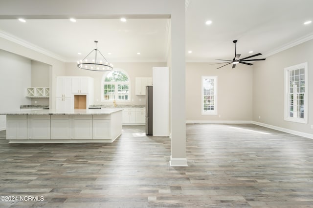 kitchen with white cabinetry, hanging light fixtures, a spacious island, light stone counters, and ceiling fan with notable chandelier