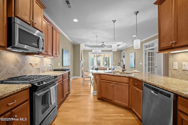 kitchen with sink, appliances with stainless steel finishes, ornamental molding, light stone counters, and hanging light fixtures