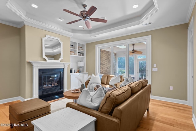 living room with a tray ceiling, ceiling fan, ornamental molding, and light hardwood / wood-style flooring