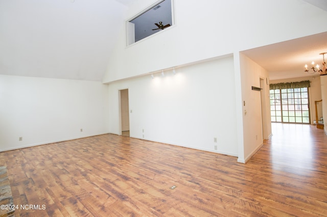 interior space featuring baseboards, high vaulted ceiling, a notable chandelier, and wood finished floors