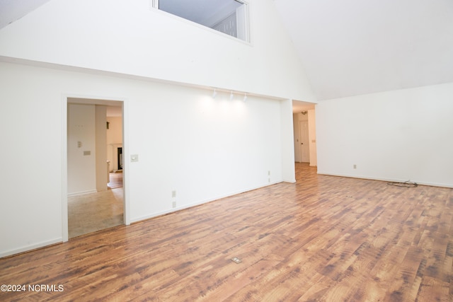 empty room with high vaulted ceiling, baseboards, and wood finished floors