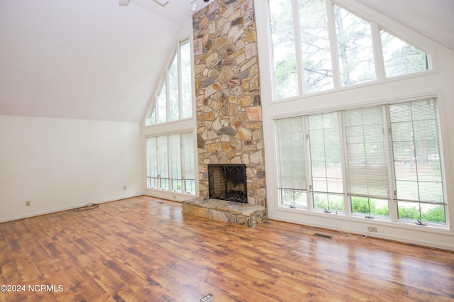 unfurnished living room featuring high vaulted ceiling, wood finished floors, a wealth of natural light, and a stone fireplace