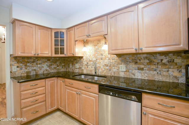 kitchen featuring stainless steel dishwasher, dark stone countertops, a sink, and decorative backsplash