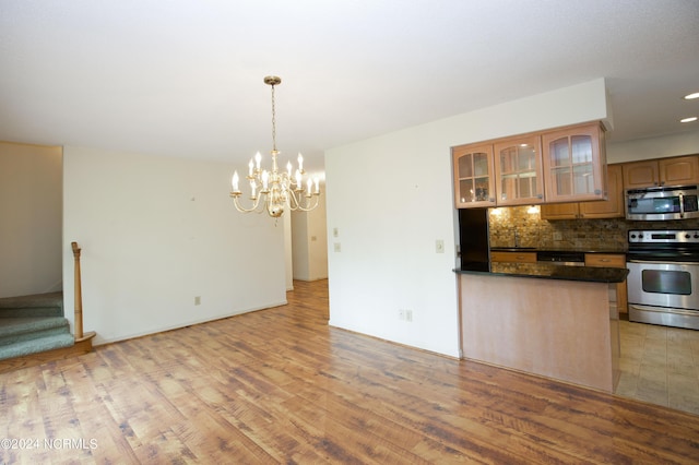 kitchen with dark countertops, decorative backsplash, appliances with stainless steel finishes, light wood-style floors, and glass insert cabinets