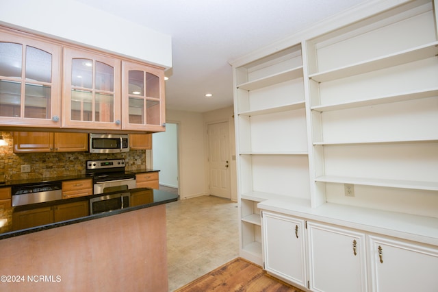 kitchen featuring open shelves, stainless steel appliances, backsplash, glass insert cabinets, and dark stone counters