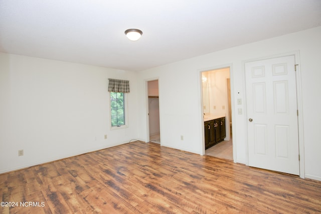 unfurnished bedroom featuring a spacious closet, light wood finished floors, and ensuite bathroom