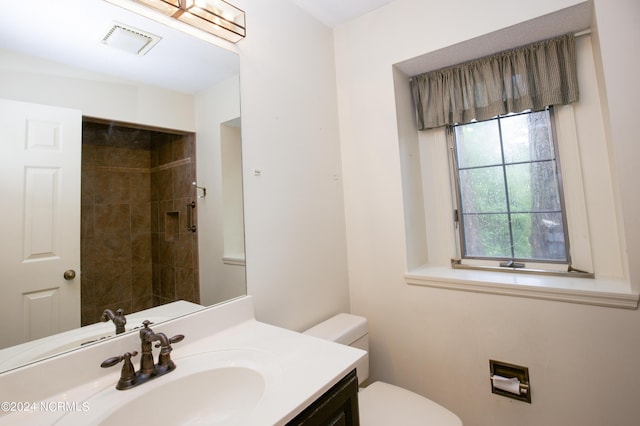 bathroom with visible vents, vanity, toilet, and tiled shower