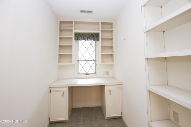 unfurnished office featuring light carpet, built in desk, visible vents, and baseboards