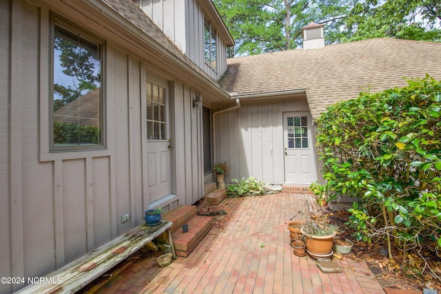 entrance to property with board and batten siding, roof with shingles, a patio, and a chimney