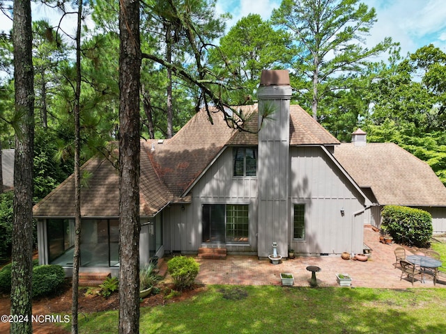 back of house featuring a yard, a chimney, a patio area, and roof with shingles