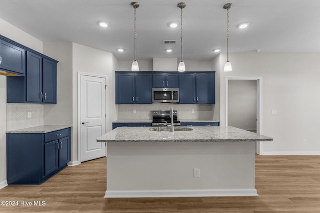 kitchen with light stone countertops, stainless steel appliances, sink, light hardwood / wood-style floors, and an island with sink