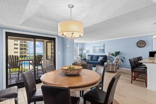 dining space with a textured ceiling, a raised ceiling, light hardwood / wood-style flooring, and an inviting chandelier