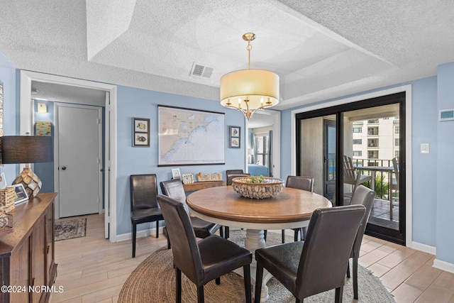 dining area featuring light wood-type flooring, a textured ceiling, a raised ceiling, and a notable chandelier