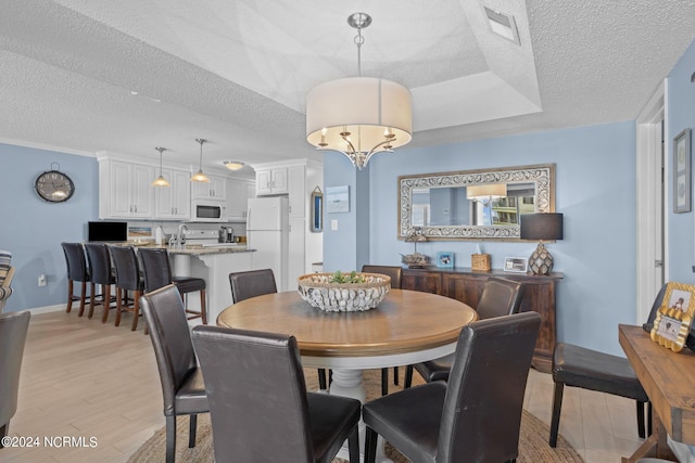 dining room featuring a chandelier, a textured ceiling, light hardwood / wood-style flooring, and a raised ceiling