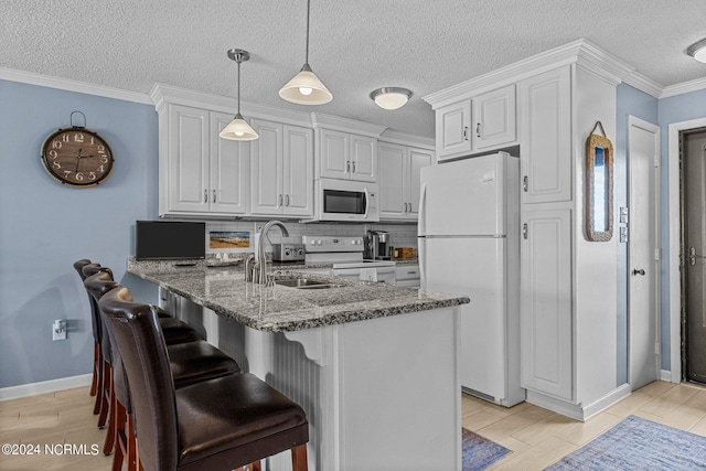 kitchen featuring white appliances, pendant lighting, kitchen peninsula, dark stone countertops, and ornamental molding