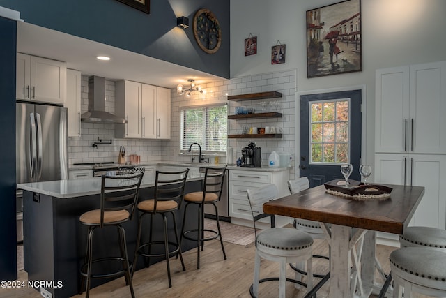 kitchen featuring light wood-type flooring, decorative backsplash, wall chimney exhaust hood, and a healthy amount of sunlight