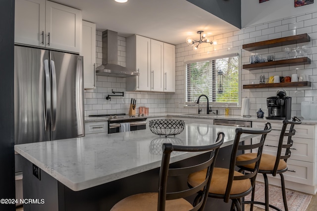 kitchen featuring wall chimney range hood, appliances with stainless steel finishes, decorative backsplash, and white cabinetry